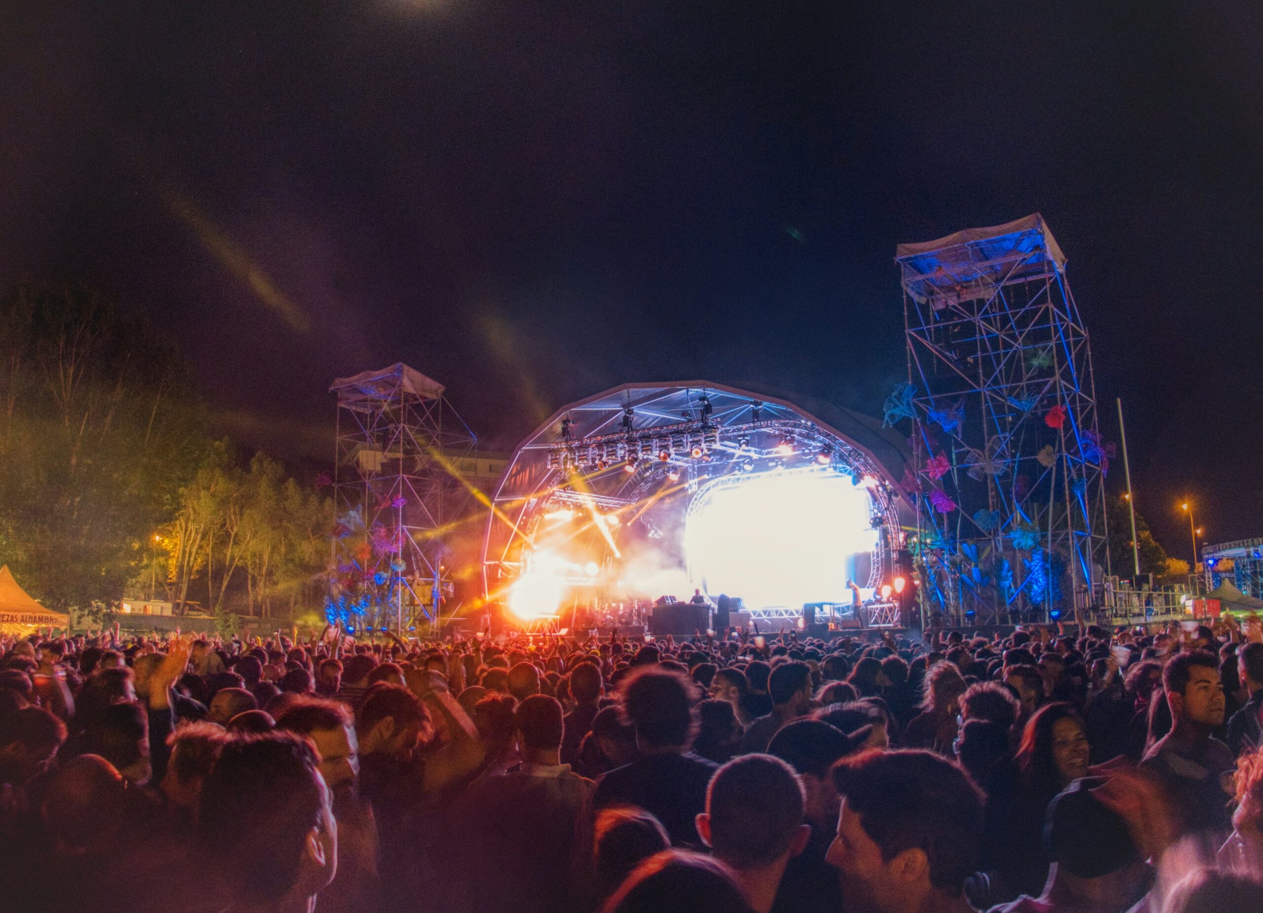 Outdoor concert stage with colourful lighting and crowd enjoying live music performance.